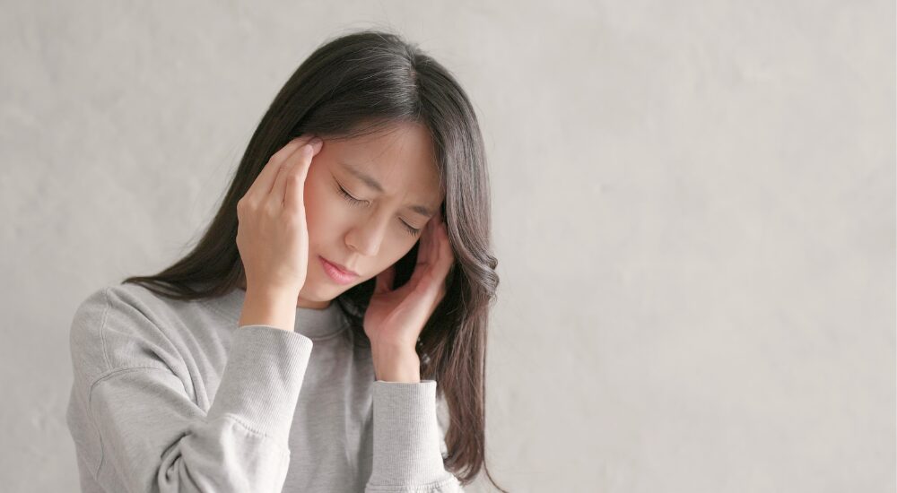 目を閉じてこめかみを押さえ、【側頭筋】や頭部の痛みにジッと耐えている状況です。ズキズキとした頭痛や眼精疲労による辛さから、「早くこの痛みから解放されたい」と悩んでいる切実な感情が伝わります。